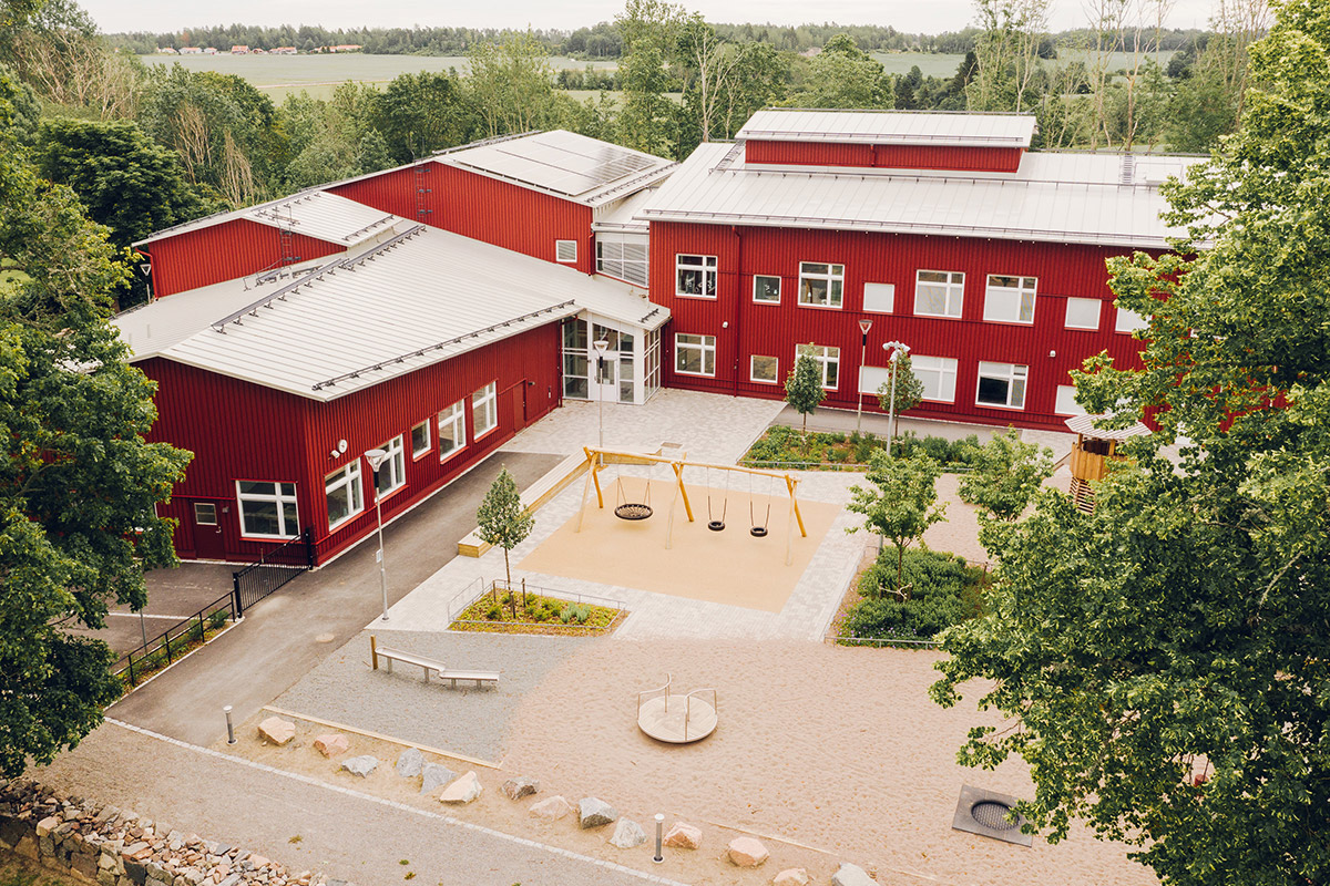 Flygbild över Jumkils röda skolbyggnader och den färdigställda skolgården med lekytor och planteringar.